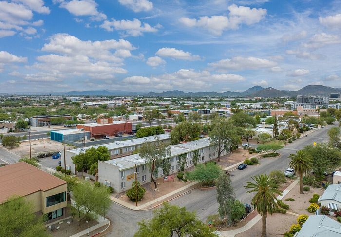 Vibrant aerial view of a charming neighborhood with lush greenery, desert landscapes, and distant mountain vistas under a picturesque sky.