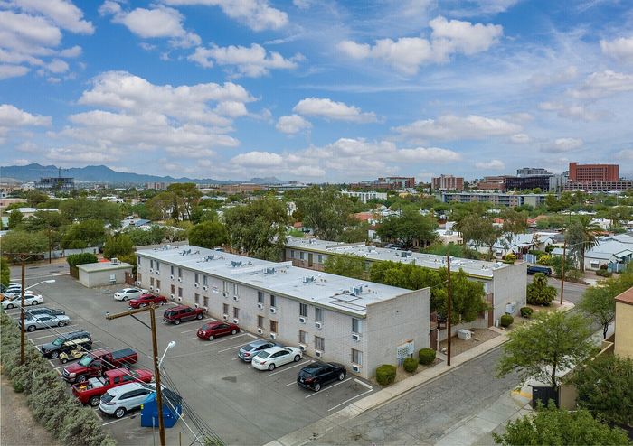 Panoramic aerial view of a charming apartment complex with convenient parking and picturesque cityscape backdrop against a vibrant blue sky.