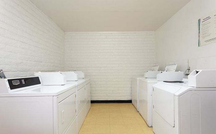 Bright and convenient laundry room with multiple washers and dryers, featuring modern appliances and a clean, spacious layout.