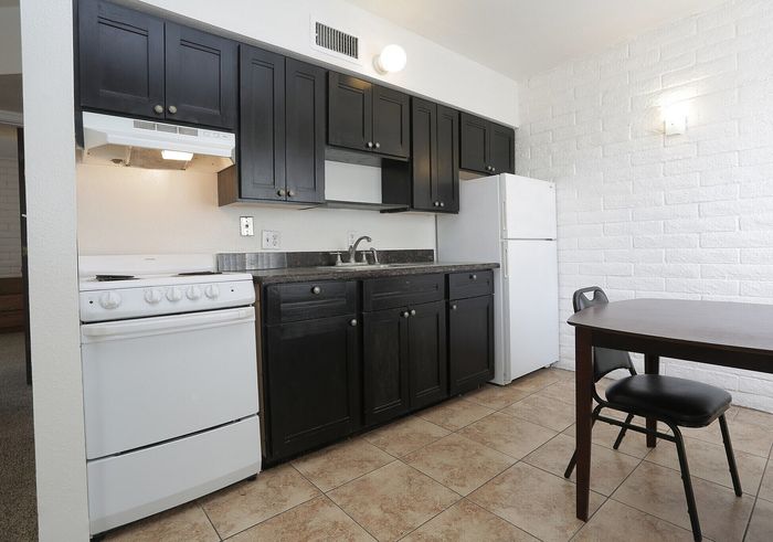 Modern kitchen with sleek black cabinets, a white stove, and a cozy dining area featuring a wooden table and chairs against a stylish brick wall.