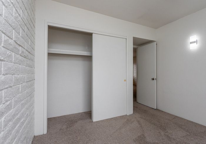 Chic bedroom with plush carpet, open closet space, and minimalist white design creating a spacious feel.