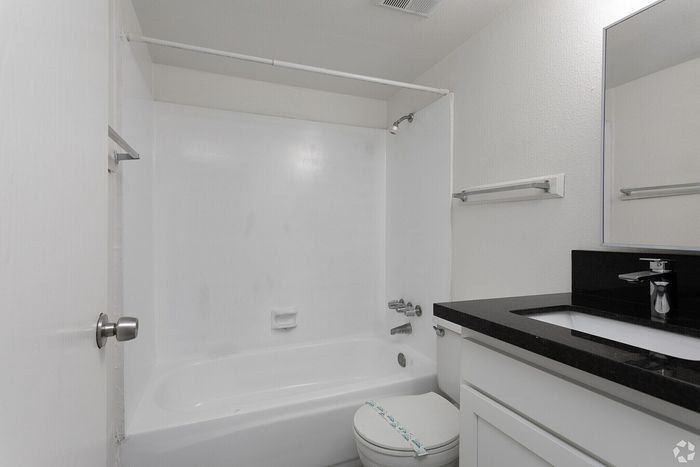 Modern bathroom featuring a sleek white bathtub, elegant black countertop, and minimalist white cabinetry.