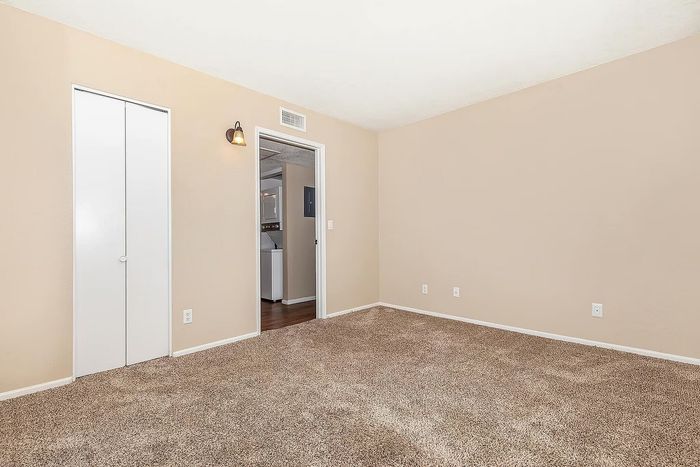 Bright and spacious bedroom featuring plush carpet, neutral walls, and stylish lighting in a modern apartment.