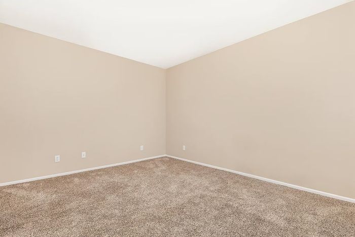 Bright and cozy room featuring soft beige walls, plush carpet, and ample power outlets, ideal for personalized decorating.