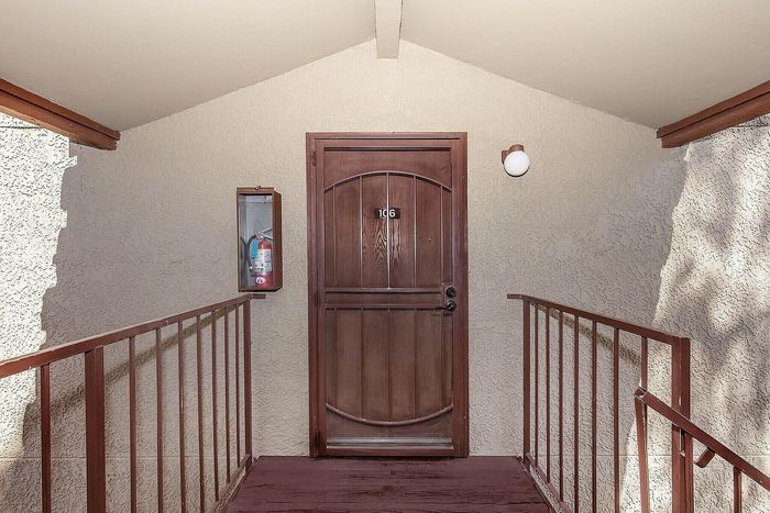 Inviting entrance to Unit 106 with a warm wooden door, well-lit setup, and a modern safety feature for peace of mind.