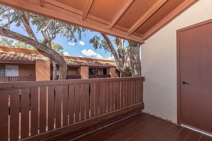 Charming balcony with wooden railings and a scenic view of rustic rooftops and lush trees, perfect for relaxing outdoors.