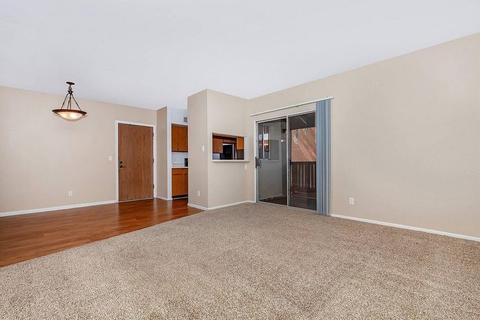 Bright and airy living space featuring elegant hardwood floors, plush carpet, and a stylish overhead light. Includes an open layout with sliding glass door leading to a private balcony.