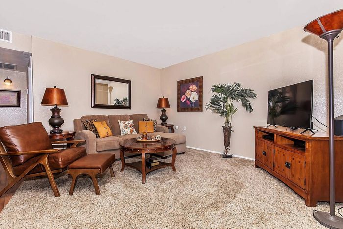 Inviting living room with plush beige sofa, stylish leather chair, and elegant wooden furniture, enhanced by vibrant decor and a large flat-screen TV.