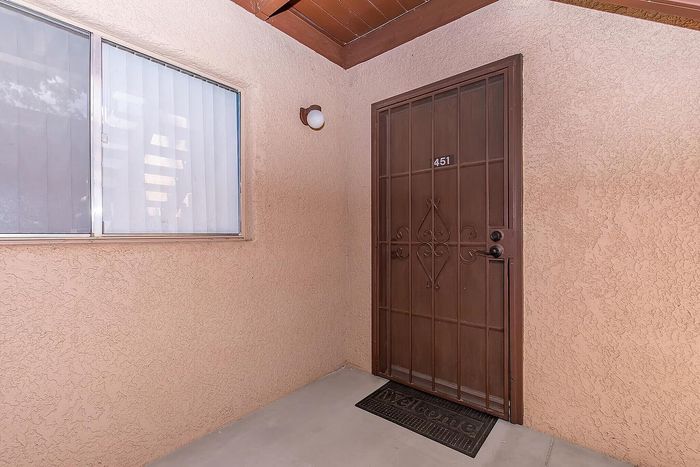Inviting apartment entrance with warm-toned stucco walls and secure metal door, complemented by a welcome mat.