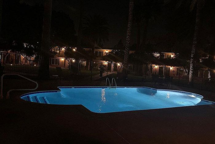 Serene nighttime view of a glowing swimming pool surrounded by illuminated apartments and palm trees.