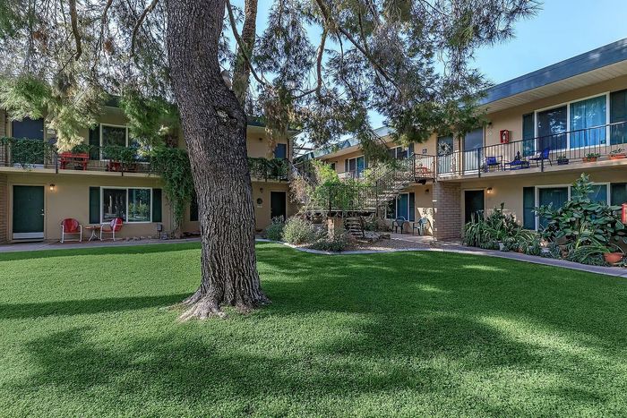 Charming garden courtyard of an apartment complex with lush greenery, vibrant plants, and cozy outdoor seating.