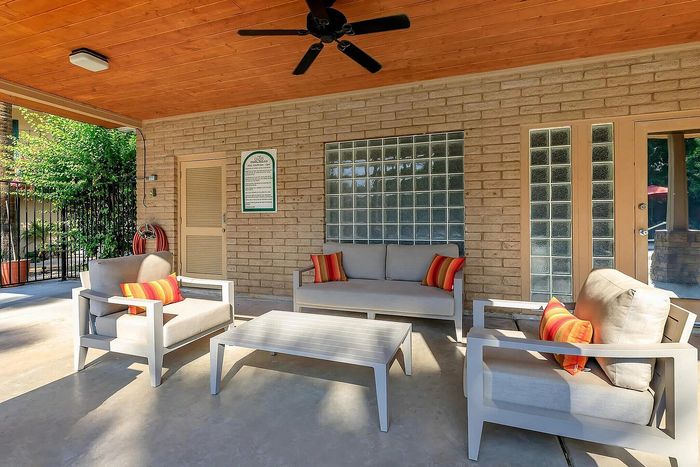 Charming patio with cozy seating, vibrant accent pillows, and natural brick wall under a warm wooden ceiling.