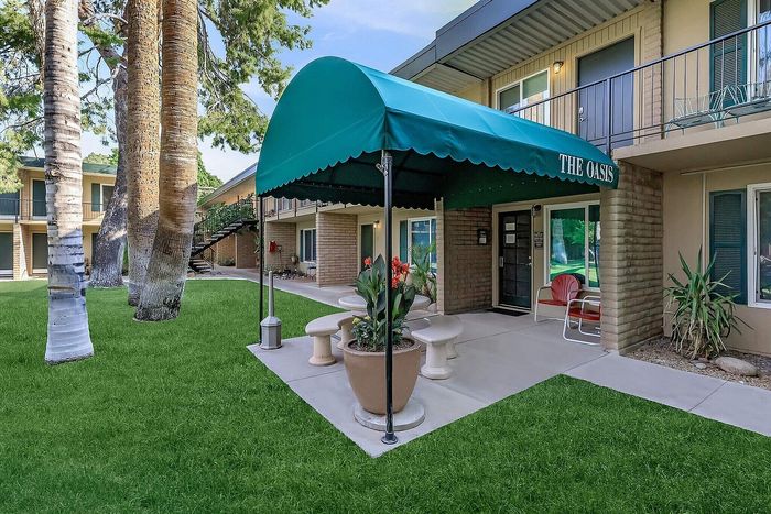 Charming apartment exterior at The Oasis, featuring lush green lawns, elegant palm trees, and a welcoming entrance with vibrant potted plants.