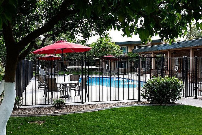 Charming apartment community with a refreshing pool, red umbrellas, and lush landscaping offering a tranquil outdoor retreat.