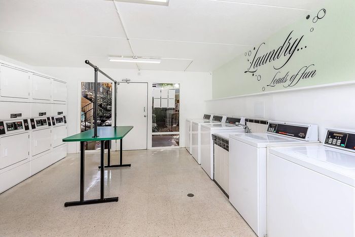 Bright and spacious laundry room with modern washers and dryers, featuring playful decor with 'Laundry... Loads of fun' signage.