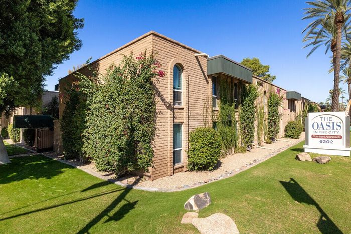 Charming brick apartment exterior with lush greenery and palm trees, showcasing 'The Oasis in the City'—a serene courtyard retreat.
