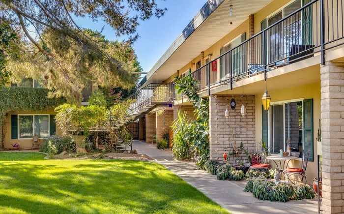 Charming apartment exterior with lush gardens, private balconies, and inviting outdoor seating areas.