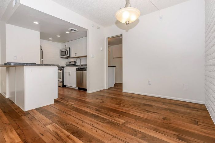 Bright and modern kitchen with stainless steel appliances and hardwood flooring, leading to an open dining area with stylish lighting.