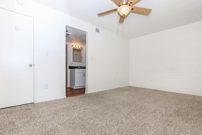 Bright and spacious room with plush carpet flooring, ceiling fan, and a doorway leading to a chic bathroom vanity area.