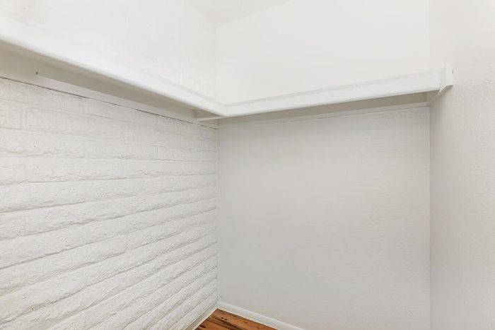 Bright, spacious closet with clean white brick walls and a wooden floor, offering ample storage space.