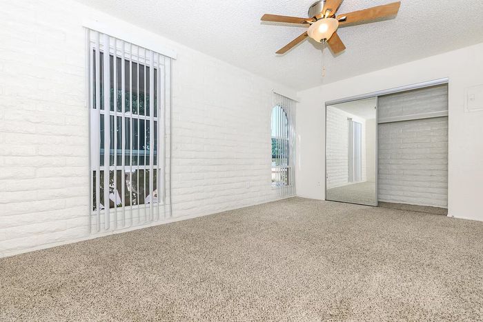 Bright and spacious bedroom with plush carpet, sliding mirrored closet doors, and modern ceiling fan.