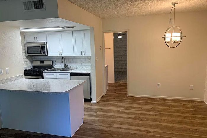 Modern kitchen with sleek white cabinets, stainless steel appliances, and elegant pendant lighting over hardwood flooring.