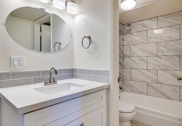 Chic modern bathroom featuring an elegant oval mirror, sleek white vanity with quartz countertop, and a stunning marble-tiled shower.