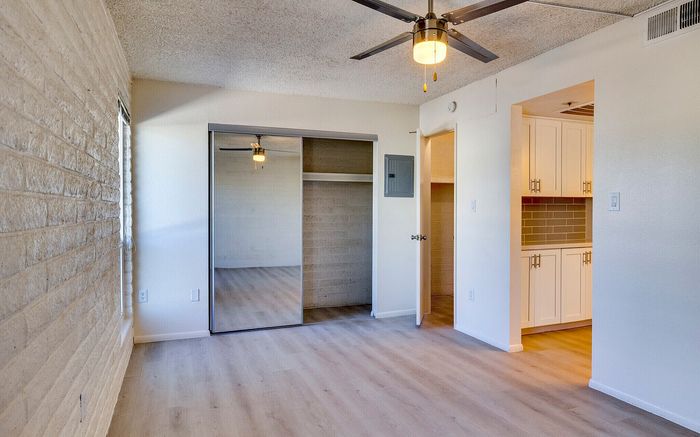 Bright and inviting bedroom with mirrored closet doors, ceiling fan, and a cozy view into a modern kitchen.