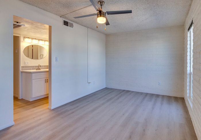Bright and inviting room with modern ceiling fan, elegant wood flooring, and a sleek bathroom vanity area.
