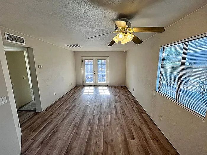 Inviting living room with elegant wood flooring, ample natural light from large windows, and a modern ceiling fan.