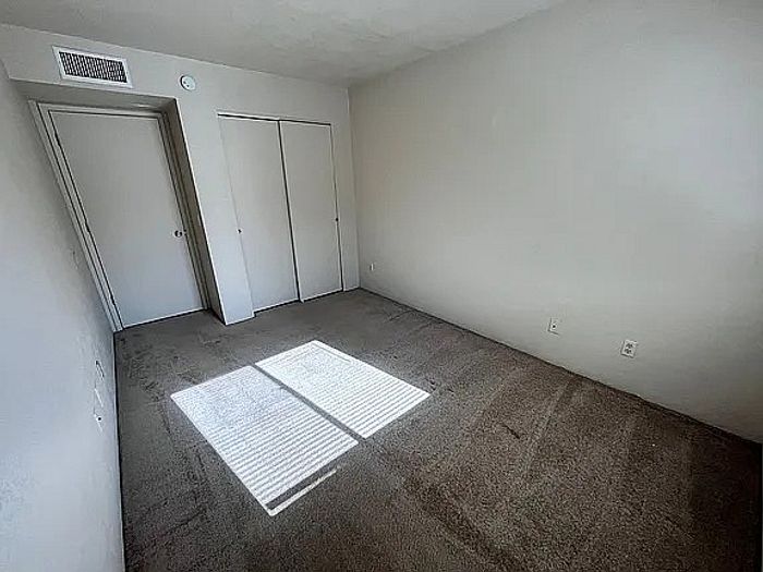 Bright, spacious bedroom with soft carpeting, ample closet space, and natural light streaming through a window, perfect for a serene retreat.