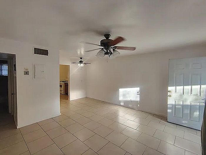 Bright and airy living space with tiled floors, ceiling fans, and a glimpse into the cozy kitchen area.