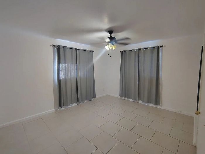 Bright and spacious room with large windows, elegant curtains, and modern ceiling fan, ideal for a comfortable living space.
