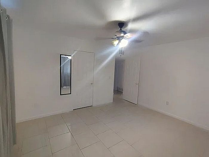 Bright, spacious room with elegant ceiling fan, tiled floor, and ample closet space enhanced by a large mirror.