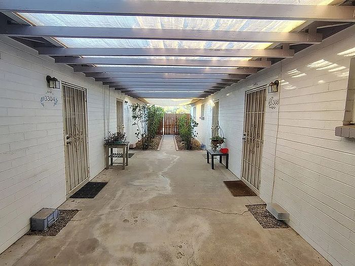 Charming courtyard corridor with pergola ceiling, showcasing inviting entrances and lush potted plants.