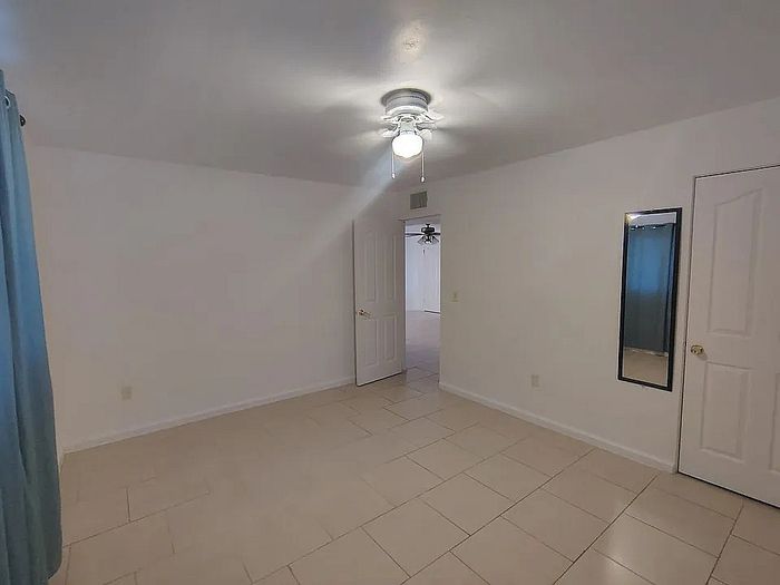 Bright and spacious room with tiled flooring, ceiling fan, and door leading to an adjoining space.