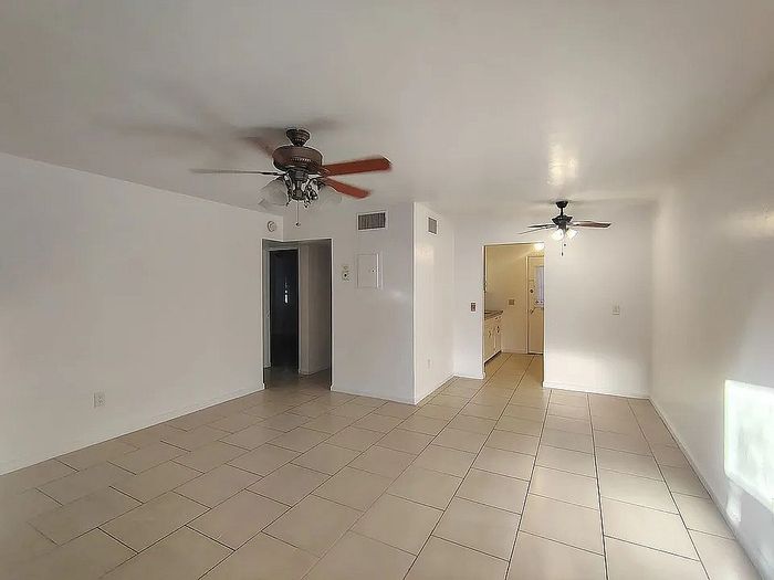 Bright, spacious living area with elegant ceiling fans and sleek tiled floors leading to a cozy kitchen.