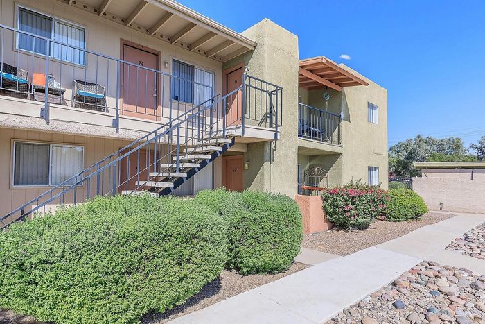 Charming apartment exterior with inviting balconies, vibrant greenery, and well-maintained walkways under a clear blue sky.