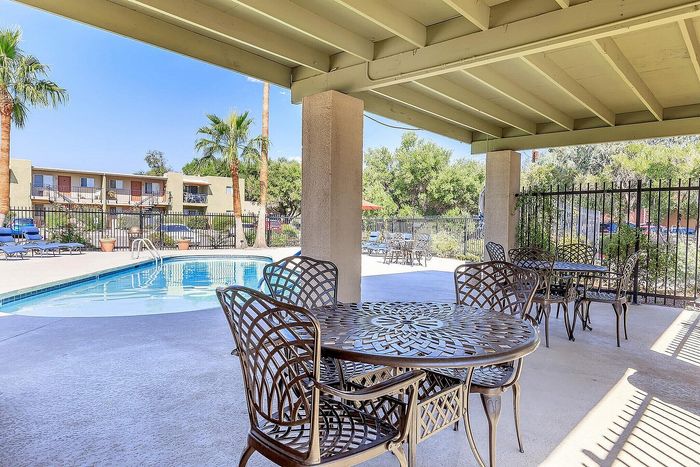 Inviting outdoor pool area with elegant wrought iron furniture, surrounded by lush greenery and palm trees, perfect for relaxation.