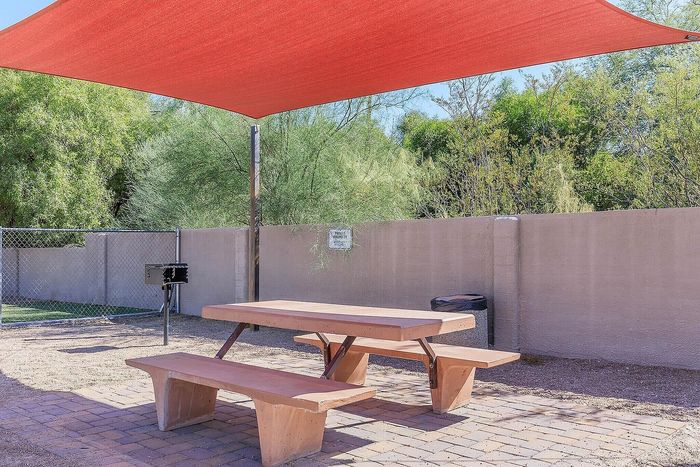 Inviting outdoor picnic area with modern red sunshade, surrounded by lush greenery for a relaxing atmosphere.