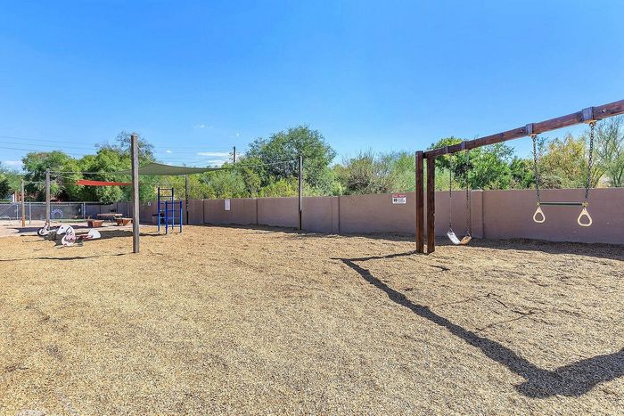 Inviting playground area featuring swings, climbing structures, and picnic tables under sun shades, perfect for family fun and outdoor relaxation.