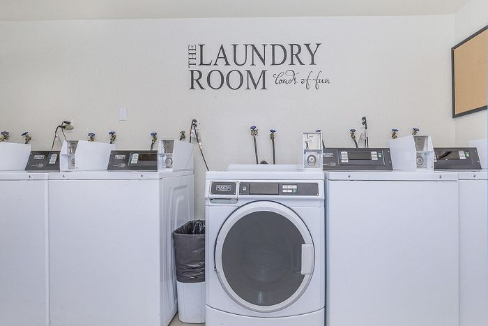 Modern laundry room featuring high-efficiency washers in a bright, inviting space with 'The Laundry Room' slogan on the wall.