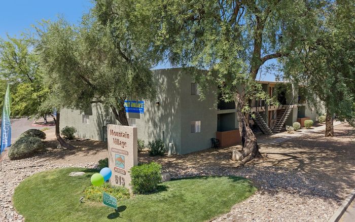 Charming Mountain Village apartments nestled among lush trees, featuring well-maintained landscaping and inviting paths.