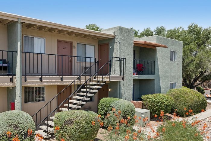 Charming apartment building with two levels, private balconies, and vibrant garden landscaping.