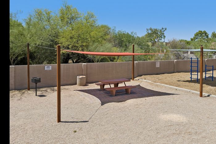 Charming outdoor area with a shaded picnic bench and grill, surrounded by lush greenery and a playground for endless family fun.