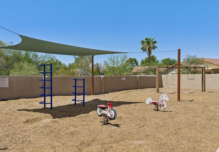 Inviting playground with climbing structures, swings, and charming spring riders under a sunshade, surrounded by lush greenery.