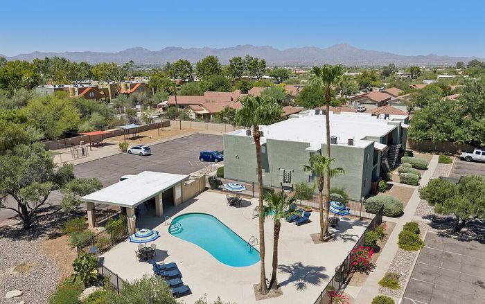 Charming apartment complex with scenic mountain views, featuring a refreshing swimming pool, outdoor patio with umbrellas, and lush landscaping.