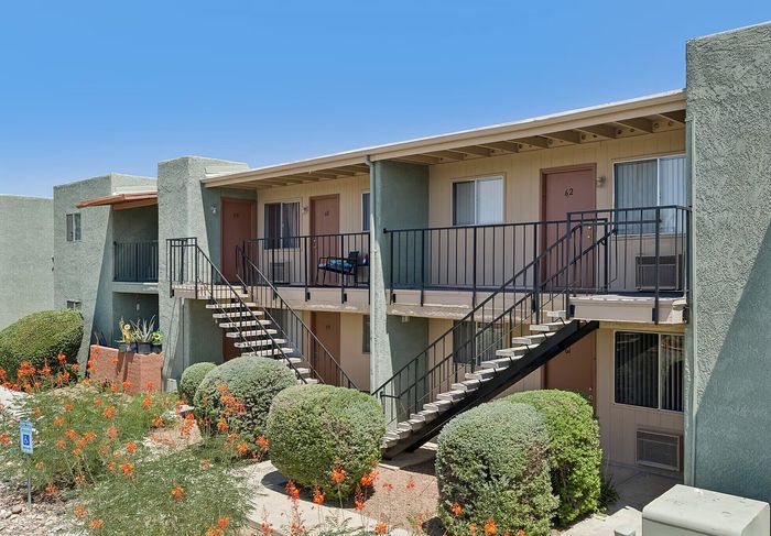 Charming two-story apartment building with spacious balconies, manicured landscaping, and vibrant flowers under a clear blue sky.
