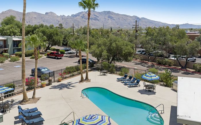 Scenic apartment view featuring a sparkling pool, relaxed sun loungers, and lush mountain backdrop.