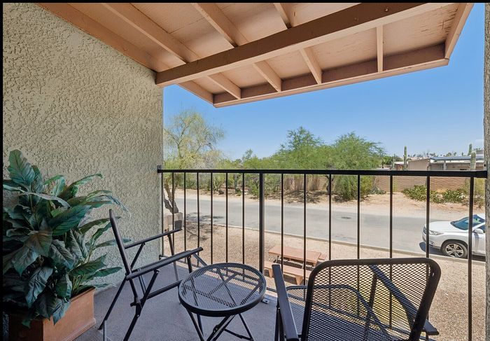 Cozy balcony with stylish outdoor seating, lush green plant, and scenic view of desert landscape.